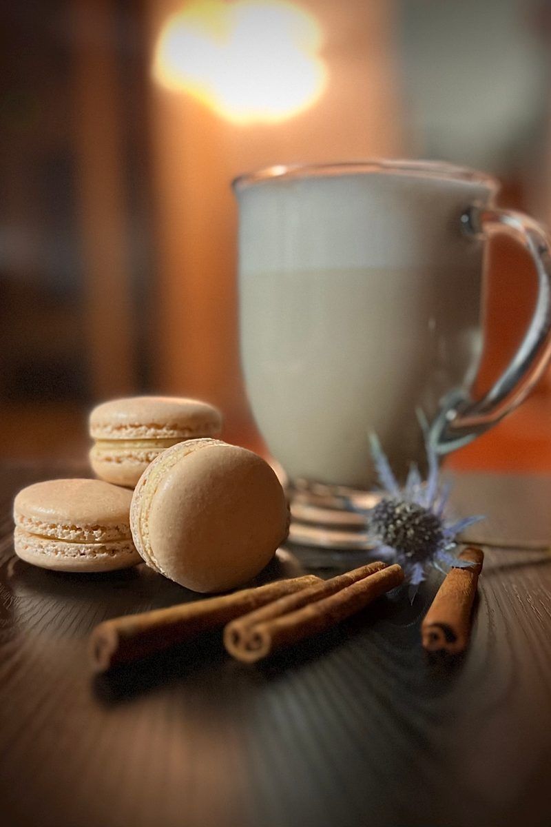 Chai macarons beside cinnamon sticks and a glass of milk