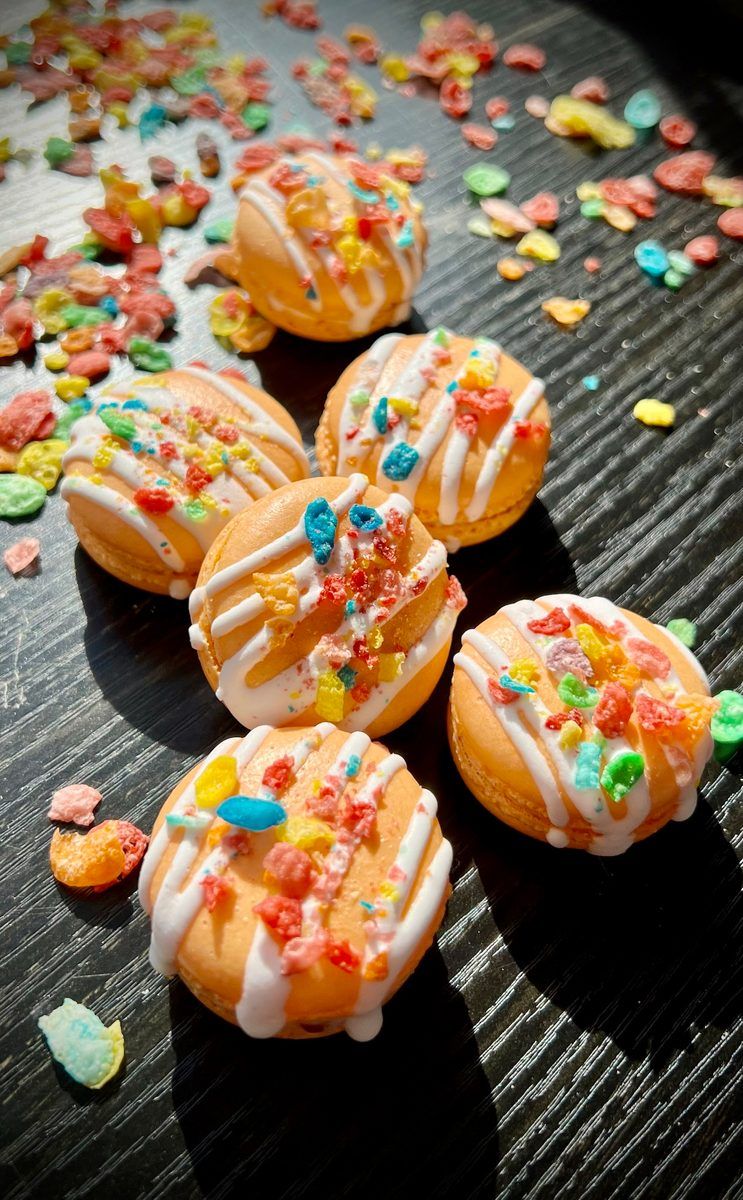 Orange macarons decorated with white drizzle and colorful Fruity Pebbles cereal