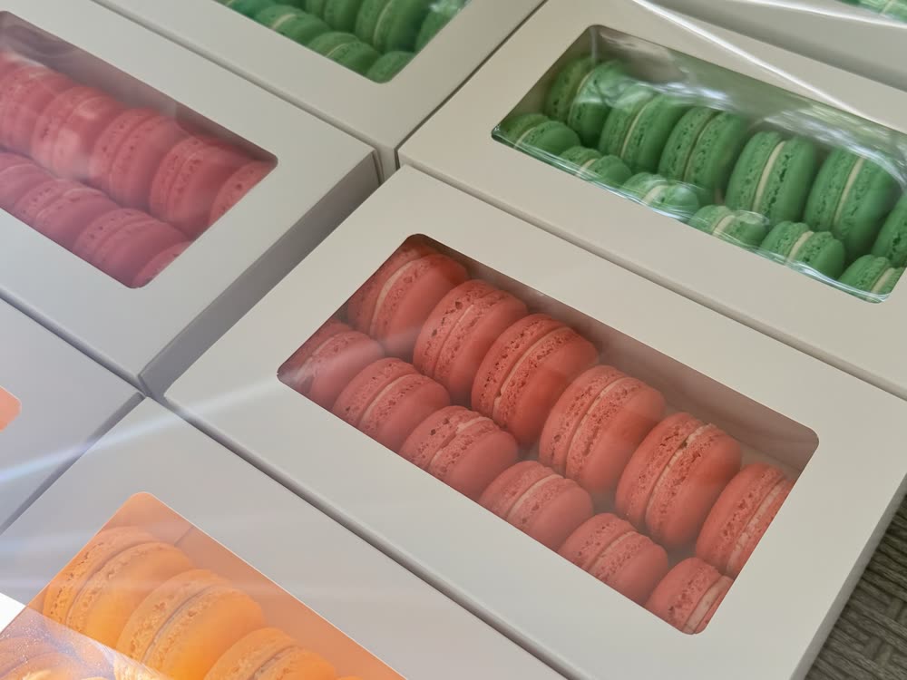 Boxes of pink, green and orange macarons laid out side by side