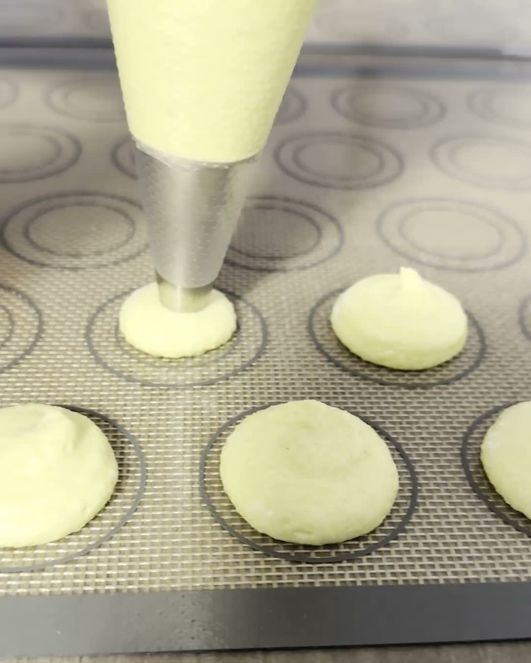 Macaron batter piped into even rounds on a silicone baking mat
